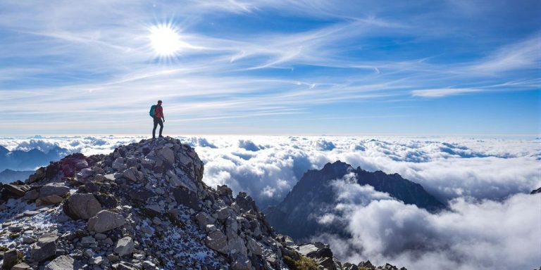Person ascending a mountain peak at sunrise.