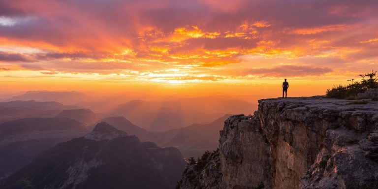 Person looking at a vibrant sunrise over mountains.