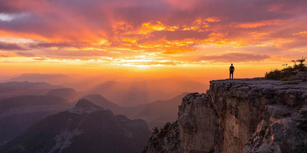 Person looking at a vibrant sunrise over mountains.