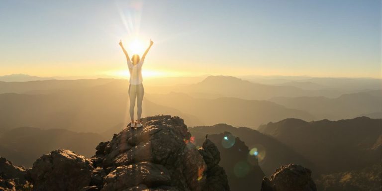 Person reaching a mountain peak at sunrise.